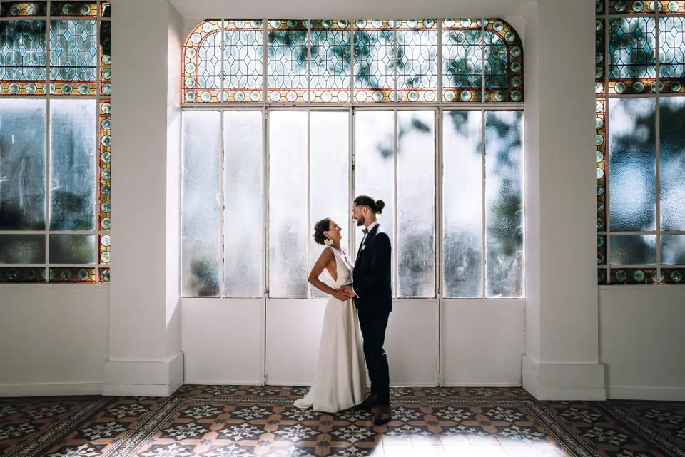 Couple de mariés posant dans la verrière lumineuse du Château La Beaumetane en Provence, moment romantique et élégant avant ou après la cérémonie